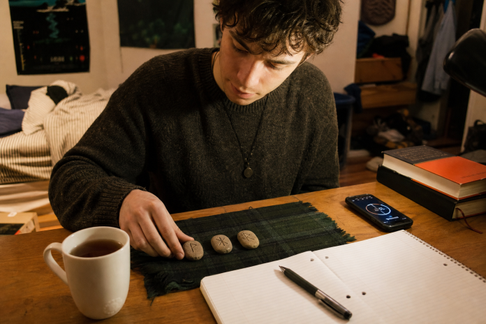 Learning to read runes: a three-rune layout at a desk Young man laying out three stone rune tiles beside a notebook at a bedroom desk