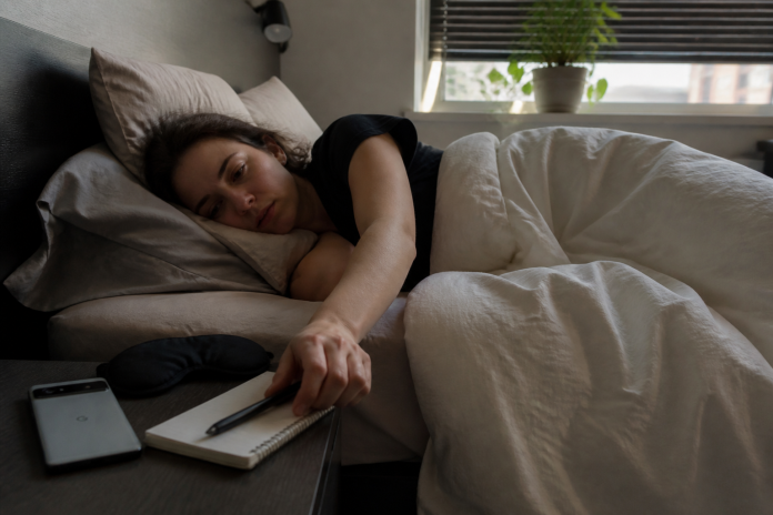 Reaching for the dream journal on waking Woman in bed reaching for a notebook on the nightstand just after waking