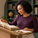 The 18 Armanen Runes: What They Are, Where They Came From, and Why to Be Careful Woman studying an open history book at an oak lectern beside a notebook and a wooden Isa rune