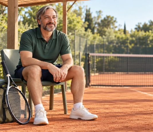 Breathwork for Athletes Under Pressure: Benefits and Safety Man seated beside a tennis court with a racket and sports bag, pausing before practice