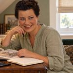 How to Know if You Lived a Past Life: The Nine “Signs”, What Each Really Is, and What the Research Says A woman with swept-up dark hair sits at a walnut writing desk with a history book, notebook and phone.