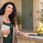 Ready for a Psychic Reading? Seven Questions and Your Choices A dark-haired woman holds a closed notebook beside a stone ledge with a phone and card box.