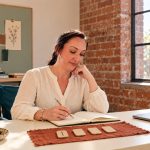 How to Ask Runes for Guidance: Questions, Reflection and Your Next Step Woman considering notes beside four wooden rune tiles on a rust-colored cloth