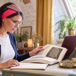 Runes History: From Iron-Age Inscriptions to a 1982 Paperback Woman comparing a history book and notebook at a sage bureau beside Isa and Gebo stones