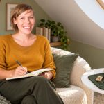 Runes and Psychic Intuition: Meaning, Reflection and Clear Boundaries Woman writing in a notebook beside wooden rune tiles in a bright attic reading nook