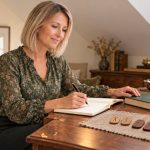 Healing Through the Runes: Symbolism, History and Medical Boundaries Woman with a straight ash-blonde bob writing beside wooden rune tiles and a book at a walnut bureau