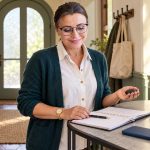 Five Symbolic Energy-Protection Tools for Empaths A woman with tied-back brown hair and glasses holds a small black stone beside a planner and a pink rose.