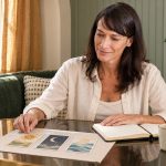 Can Tarot Cards Tell You He’s Cheating? What the Cards Can and Cannot Do A dark-haired woman reflects on three illustrated cards beside an open notebook in a window alcove.