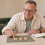 What are runes? Man with gray hair and glasses examining three wooden rune tiles beside a notebook and laptop